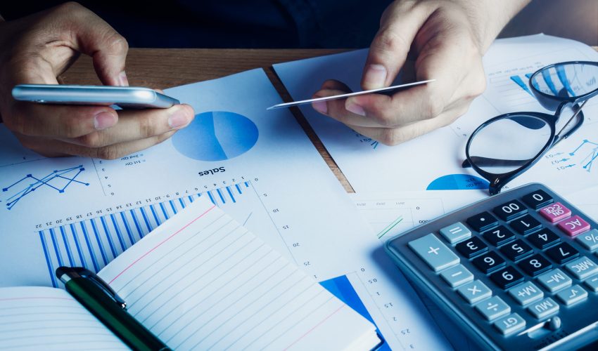 Asian hand man using mobile phone and credit for e commerce online on home office.accessories  document chart notebook eyeglasses pen on wood table background.shopping online.financial.saving concept.