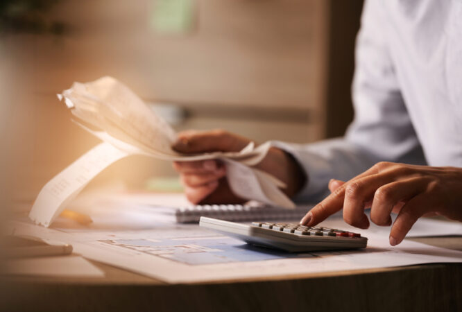 Close-up of economist using calculator while going through bills and taxes in the office.