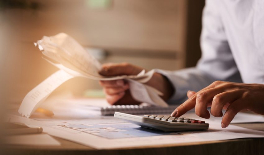Close-up of economist using calculator while going through bills and taxes in the office.