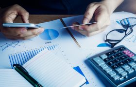 Asian hand man using mobile phone and credit for e commerce online on home office.accessories  document chart notebook eyeglasses pen on wood table background.shopping online.financial.saving concept.