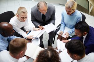 Circle of contemporary business people with documents having discussion of their reports at briefing